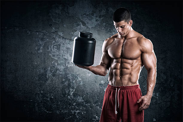 Studio portrait of male fitness athlete perfectly shaped and muscle toned wearing red shorts and holding a can of supplements.